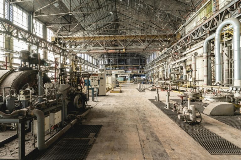 Spacious industrial warehouse interior featuring machinery and network of pipes.